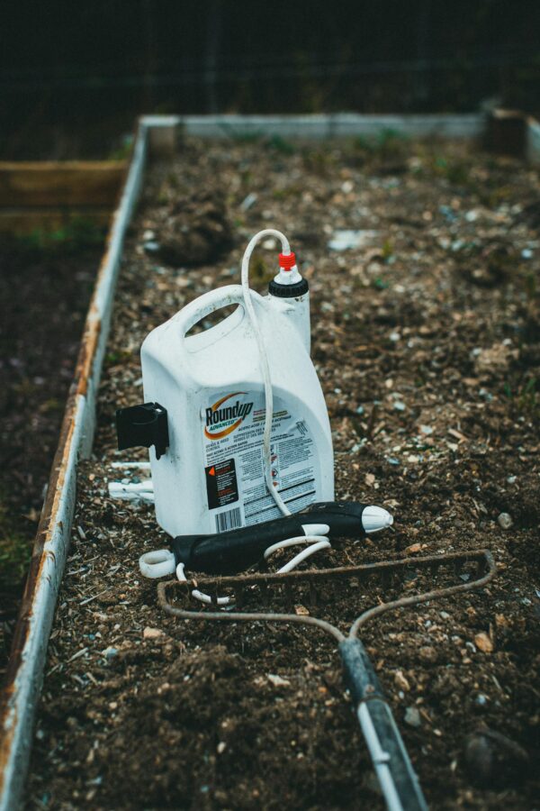 Close-up of a garden spray container on soil in a raised bed, ready for gardening.